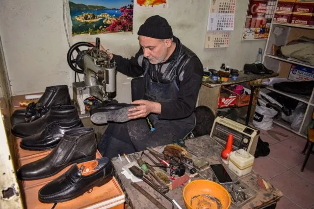 Meșteri care repară încălțăminte la o masă de lucru, cu unelte și cizme așezate în jur